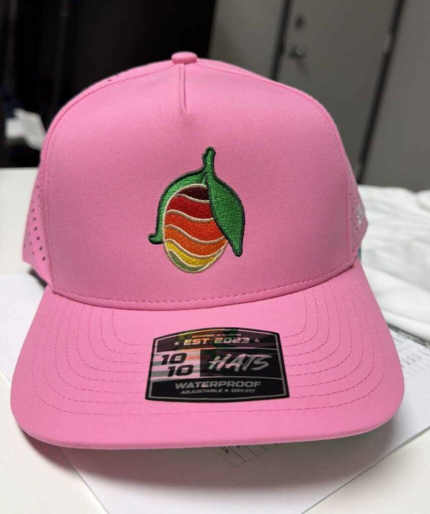 High color custom embroidered mango logo on a pink performance trucker hat
