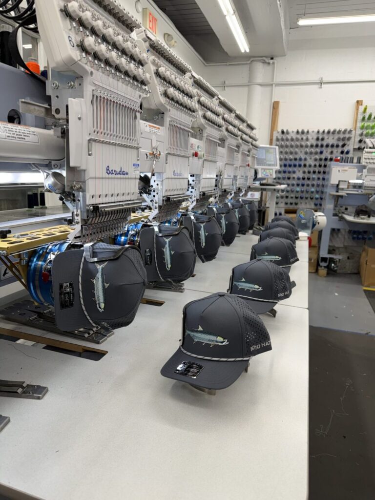 Barudan multi-head commercial embroidery machines running a bulk custom hat order with tarpon fish logo